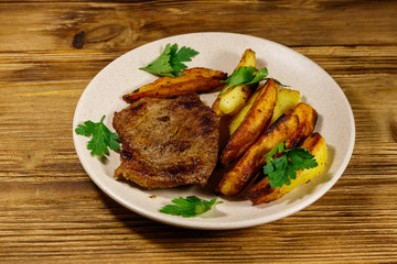 Fried beef steak with potato wedges on wooden table