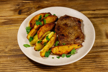 Fried beef steak with potato wedges on wooden table