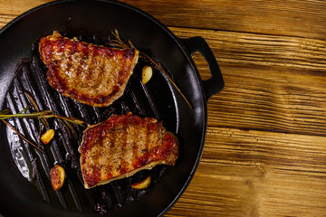 Grilled pork steaks with rosemary, garlic and spices in cast iron grill frying pan on wooden table....