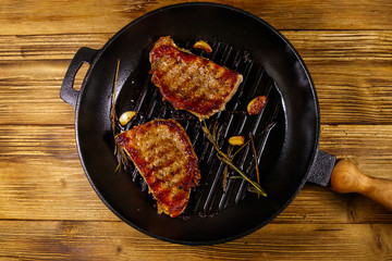 Grilled pork steaks with rosemary, garlic and spices in cast iron grill frying pan on wooden table. Top view