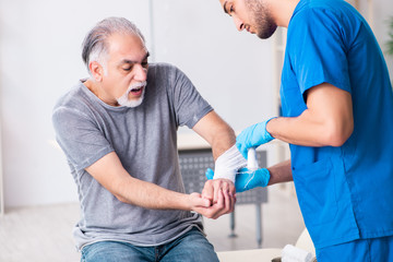 Young male doctor and old patient in first aid concept
