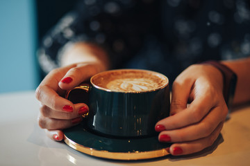 Hands holding a green mug standing on a table close-up blurred background