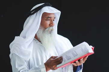 Elderly Muslim Arabic man reading the holy book Quran, black background