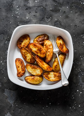 Roasted new potatoes in baking dish on a dark background, top view. Delicious snack, tapas