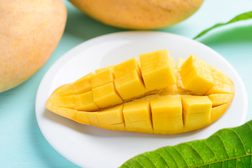 Ripe mango fruit sliced to cubes on white plate and leaf on pastel color background, tropical fruit