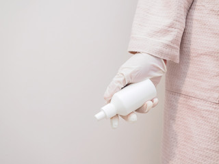 A hand in a rubber glove holds a white plastic bottle, mock up, copy space. Disinfection and precautions during a coronavirus pandemic. Protecting your hands from the virus in an epidemic