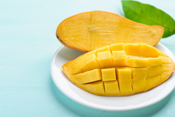 Ripe mango fruit sliced to cubes on white plate and leaf on pastel color background, tropical fruit