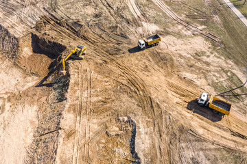 top down view of an excavator and dump trucks working on construction site