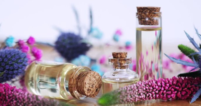 Floral aroma liquid parfume in transparent bottles, essential oil in glass vial. Fresh purple and pink flowers with bottles and cork caps on wooden background. Production of perfume, scent, fragrance.