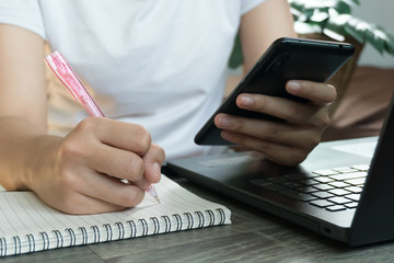 Young business woman sitting at table with laptop and taking notes in notebook.