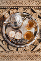 Traditional moroccan mint tea with cookies on silver tray on carved wooden table. Beautiful vintage style, hospitality in Morocco.