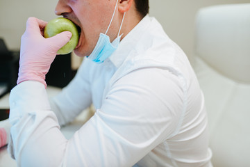 A businessman with gloves on his hands eats an apple. COVID - 19 virus protection