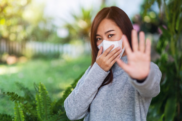 Closeup image of an asian woman wearing protective face mask, making stop hand sign for preventing the spread of Covid-19 the pandemic concept
