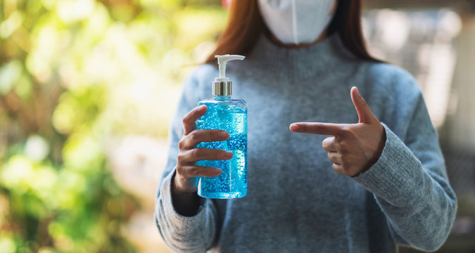 Closeup image of a woman wearing protective mask holding and pointing finger at a bottle of alcohol gel sanitizer for Healthcare and Covid-19 or 2020 virus concept