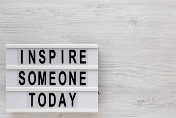 'Inspire someone today' words on a lightbox on a white wooden background, top view. Overhead, from above, flat lay. Copy space.
