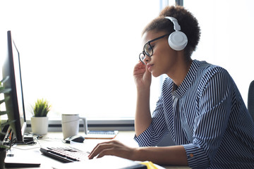 Young african american woman having a break and listening music in headphones sitting on working...