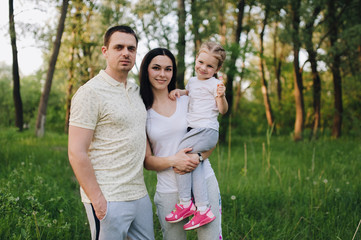 Portrait of a happy family in nature. A guy, a girl and a little daughter are hugging, standing in tracksuits in a green flowered garden and forest. Photography, concept.