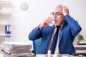 Old male sick employee working overtime in the office
