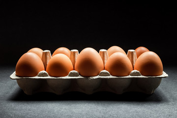 Chicken eggs in a carton on dark grey background, natural light coming from above, horizontal moody photo with deep shadows