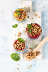 Vegan blue spirulina chia puddings with jam and granola in glass jars on a light blue table. Concept of healthy eating, dieting, fitness menu. Various layered dessert for breakfast. Top view.