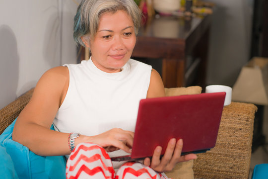 Attractive And Happy Middle Aged Woman On Her 50s Working On Laptop Computer At Living Room Couch Relaxed As Independent Entrepreneur And Internet Business Success