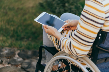 Fashionably dressed woman in a wheelchair with a modern tablet in hand walks on the street.