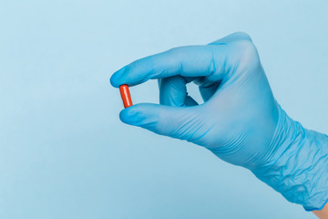 A hand in a blue medical glove holds one pill on a blue background. Disease Prevention Treatment
