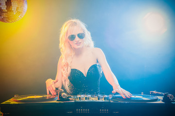 Beautiful blonde DJ girl in a white suit on decks on the party on the black background