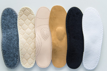 Studio photo of orthopedic insoles. A variety of orthopedic insoles are laid out in a row. Different colors and coatings: leather, cotton, microfiber.