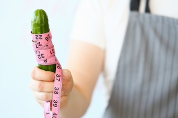 Abstract close-up woman hand diet concept with cucumber and measure tape. Female character with...