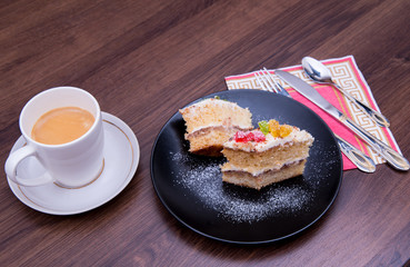 Cake on a black plate, with a mug of coffee, cutlery on the table