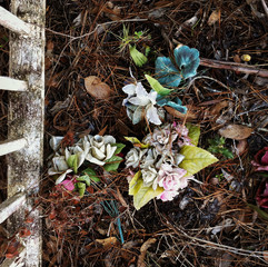 Looking down onto aged and faded plastic flowers lying on a grave in an overgrown cemetery