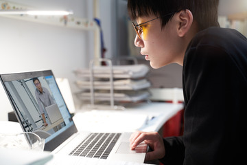 Asian kid learning from home on laptop in his bedroom during covid-19 quarantine