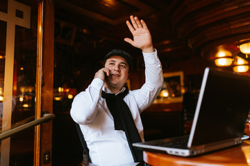 
A young caucasian handsome businessman sits in a cafe talking on the phone in front of a laptop