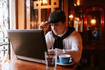 Fototapeta premium A young caucasian businessman sits in a cafe and works at a computer. Business man working and sitting by window
