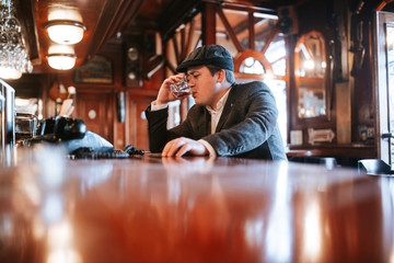 
A young man with a cap sits at a bar and drinks whiskey. Business man sitting in cafe after work