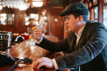 
A young man with a cap sits at a bar and drinks whiskey. Business man sitting in cafe after work