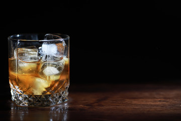 A glass of strong alcoholic drink with ice on a wooden bar counter. Whiskey with ice cubes. Glass with a chilled drink.