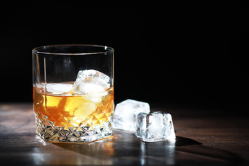 A glass of strong alcoholic drink with ice on a wooden bar counter. Whiskey with ice cubes. Glass with a chilled drink.