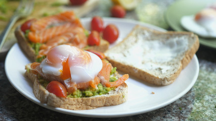 Cutting toast with pouched egg, salmon and avocado on a white plate. Cooking healthy toast with salmon and tomato