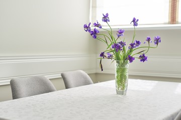 Bright dining room interior, table and chairs near window, bouquet in vase