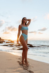 Portrait of attractive blonde girl with long hair posing on beach on sunset background.