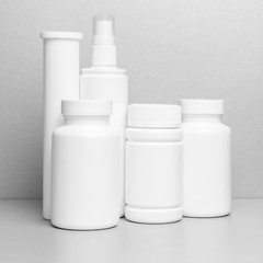 6 white vials without labels for medicines, vitamins, sprays, liquids are on a gray shelf. mockup for pharmacy and store design