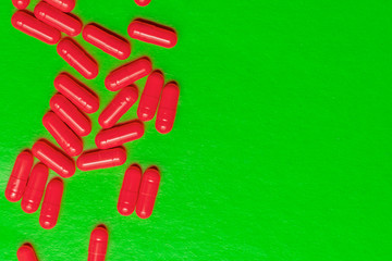 scattering of bright red pills on a green background. copy space on the left, layout for the branches of nutrition, medicine