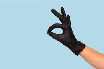 Hand in black medical glove shows OK sign on a blue background.