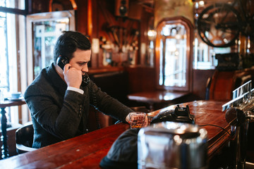 
A young man sits at a bar and talks on an old phone. Business man sitting in cafe after work