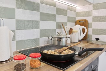 The meat is fried in pan on hob. Kitchen interior, cooking utensils background