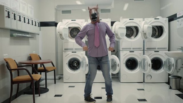 Joyful Man in mask horse Dancing Cheerful In Laundry Room. Man Dancing Viral Dance And Have Fun In Laundry Room. Happy Guy Enjoying Dance, Having Fun Together, Party Halloween. Slow Motion. Halloween