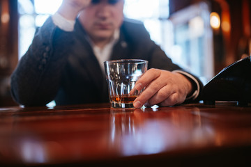 
A young man with a cap sits at a bar and drinks whiskey. Business man sitting in cafe after work