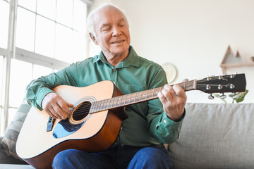 Elderly man playing guitar at home - Powered by Adobe